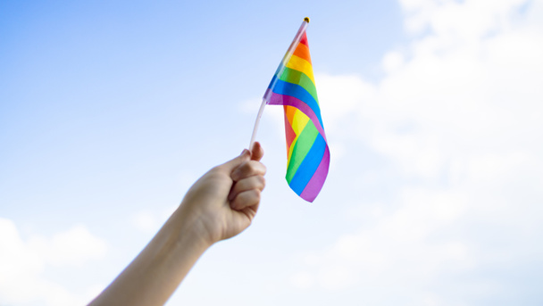 Społeczność LGBT. Mała flaga lgbt w dłoni przeciwko błękitnemu niebu - Zdjęcie, obraz