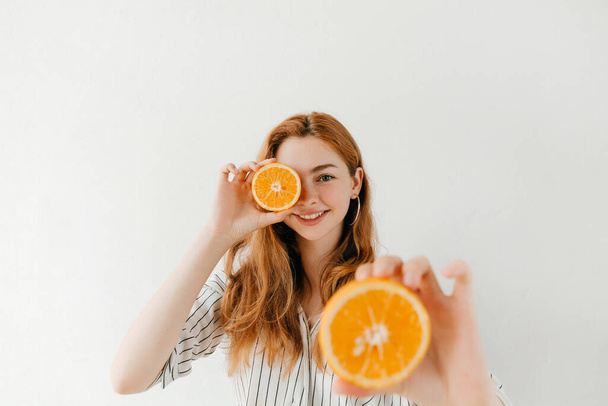 Uśmiechnięta, atrakcyjna dziewczyna trzymająca wycięty pomarańcz na białym. Idealny owoc na zimę - Zdjęcie, obraz