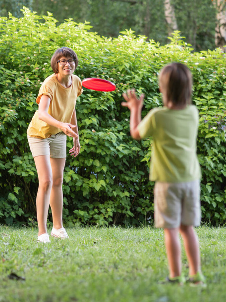 Mother and son play frisbee on grass lawn. Summer vibes. Outdoor leisure activity. Family life. Sports game at backyard. - Foto, imagen