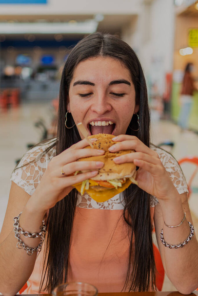 A beautiful young woman is eating a burger with cheddar. - Φωτογραφία, εικόνα