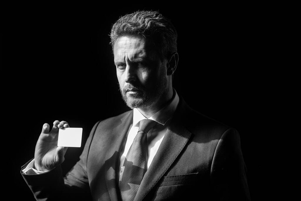 Großaufnahme Porträt eines erfolgreichen Geschäftsmannes mittleren Alters mit Kreditkarte im Anzug auf schwarzem Hintergrund. Geschäftsmann mit selbstbewusstem Gesicht. - Foto, Bild