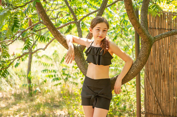 Ένα έφηβο κορίτσι 10 ή 11 ετών στέκεται κοντά σε ένα δέντρο το καλοκαίρι. Ανάπαυση, καλοκαίρι. - Φωτογραφία, εικόνα