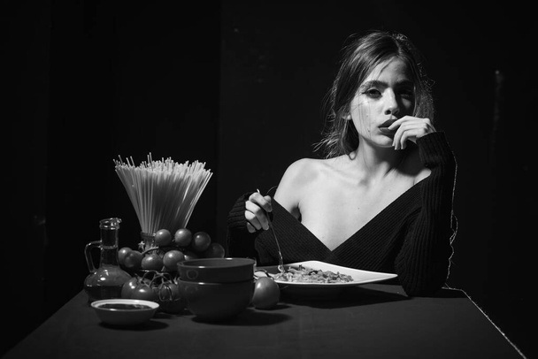 Gorgeous young brunette woman having Italian food. Seductive cheeky girl with plate of pasta eats pasta with ketchup. - Foto, imagen
