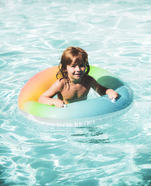 Happy kid playing with colorful swim ring in swimming pool. Child water toys. Children play in tropical resort. Family beach vacation and summer activity. - Foto, Imagem