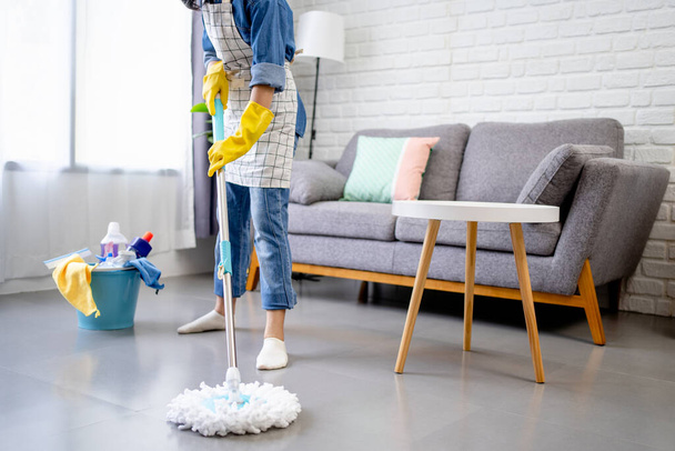 Jonge vrouw met een vloer wisser en vegen vloer, het houden van de dagelijkse hygiëne thuis en het doen van huishoudelijk werk. - Foto, afbeelding