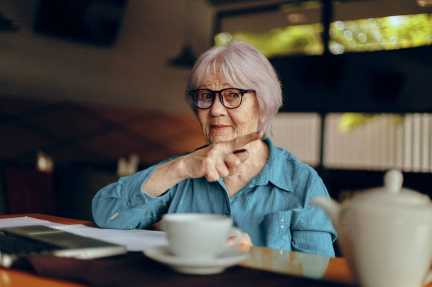 Gözlüklü yaşlı bir kadın dizüstü bilgisayarın önünde oturuyor. Hayat tarzını değiştirmemiş. - Fotoğraf, Görsel