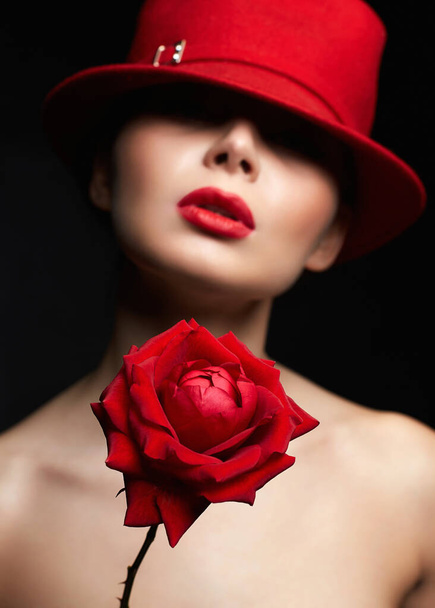 красива жінка в капелюсі за червоною трояндою. Прекрасна дівчина з макіяжем і квітковим портретом
 - Фото, зображення
