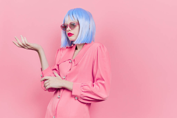 portrait of a woman in sunglasses wears a blue wig makeup pink background - Фото, изображение