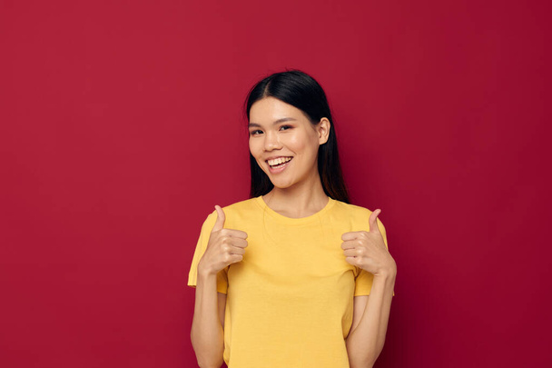 woman with Asian appearance gestures with his hands in a yellow t-shirt casual wear red background unaltered - Fotó, kép
