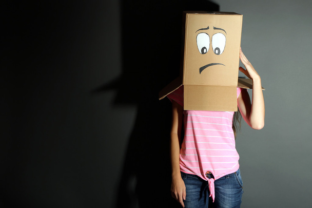 Woman with cardboard box on her head with sad face, on grey background - Fotó, kép