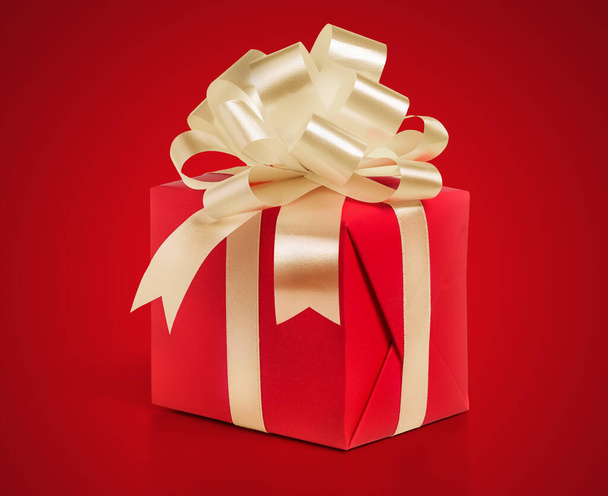 Cadeau doos verpakt in een rood papier met gouden strik op een rode achtergrond. - Foto, afbeelding