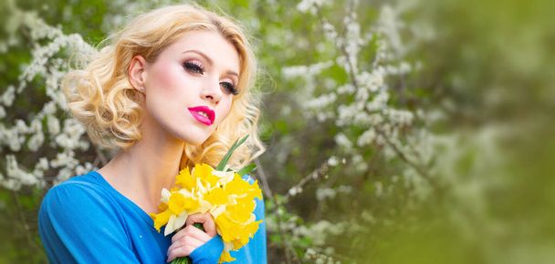 Spring woman face for banner. Close-up portrait of a beautiful young woman with curly blonde hair, perfect skin and beautiful make up in a pink floral summer garden. - Foto, Bild