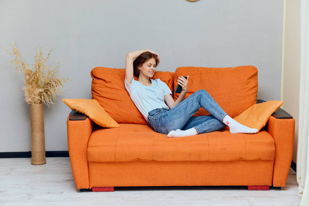 woman resting on orange sofa next to phone technology - Zdjęcie, obraz