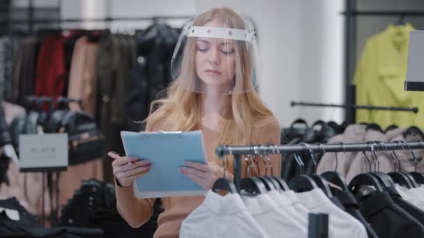 Καυκάσιος κορίτσι πωλητής ρούχα διευθυντής κατάστημα κάνουν απογραφή ρεκόρ επιτυχημένη πωλήτρια γυναίκα σε διαφανή μάσκα σταθεί σε εσωτερικούς χώρους σοβαρό ιδιοκτήτη boutique ρεκόρ πληροφορίες σχετικά με την έκπτωση προϊόν - Πλάνα, βίντεο