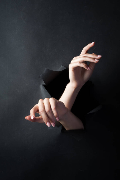 Weibliche Hände auf schwarzem, zerrissenem Hintergrund. Ein Mädchen in Dessous posiert für die Kamera. - Foto, Bild