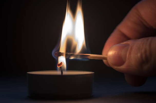 Hand lights a candle on a black background - Фото, изображение