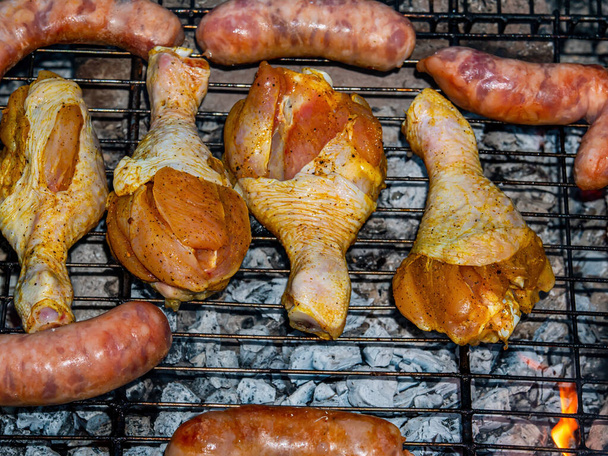 Chicken legs and meat sausages on an iron grill mesh. - Photo, Image