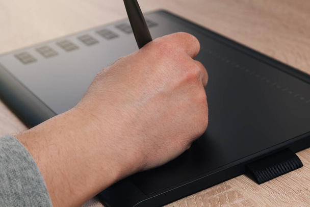 De hand van een onbekende man die tekent met een grafische tablet met een elektronisch potlood. Aan de linkerkant van de tablet zijn knoppen zichtbaar. - Foto, afbeelding