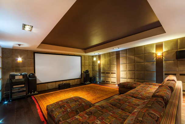 The interior of a home theater with sound-absorbing beige walls, a wide screen and a large soft sofa. - Fotoğraf, Görsel