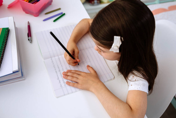Дівчина робить домашнє завдання, сидячи за столом
 - Фото, зображення