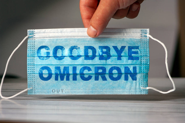 The hand holds a medical and protective mask with the word GOODBYE OMICRON. Concept of coronavirus quarantine. Prevent or stop the spread of the COVID-19 worldwide. - Fotó, kép