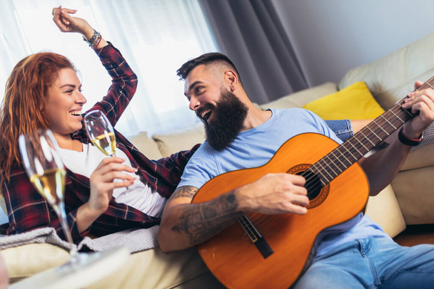 Couple is spending romantic moments together. The man is playing the guitar with his beloved girlfriend. - Фото, изображение