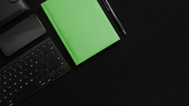 Flat lay composition with black pen, computer keyboard, smartphone, smart watch, leather wallet and bright green notebook on dark black surface. Green business concept. Business people items. Free space for text. - Zdjęcie, obraz