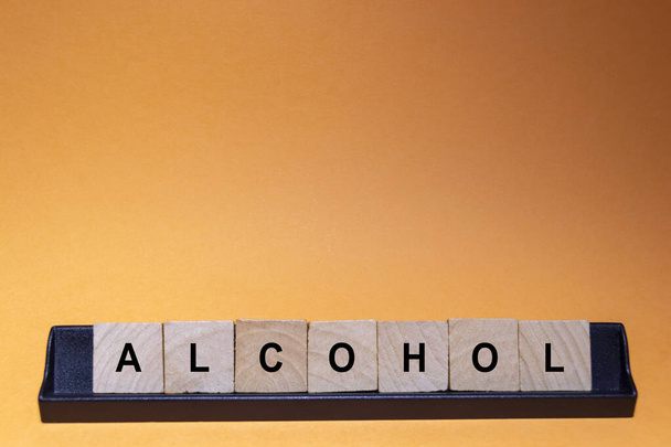 ALCOHOL. Word written on square wooden tiles with an orange background. Horizontal photography. - Photo, Image