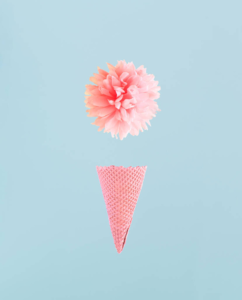 Knuspriger Waffelkegel und rosa Blume vor himmelblauem Hintergrund. Minimale Federzusammensetzung.  - Foto, Bild