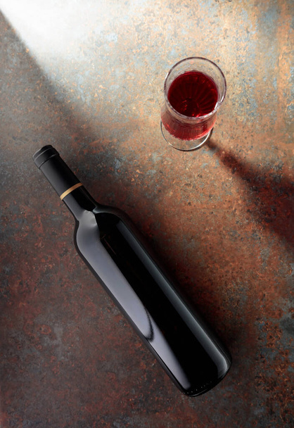 Glass and bottle of red wine on a rusty metal background. Top view with copy space. - Фото, изображение