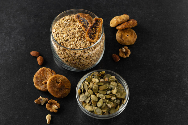 Products for a healthy breakfast, rolled oat groats with dried fruits, nuts and pumpkin seeds on a dark gray background - Fotografie, Obrázek