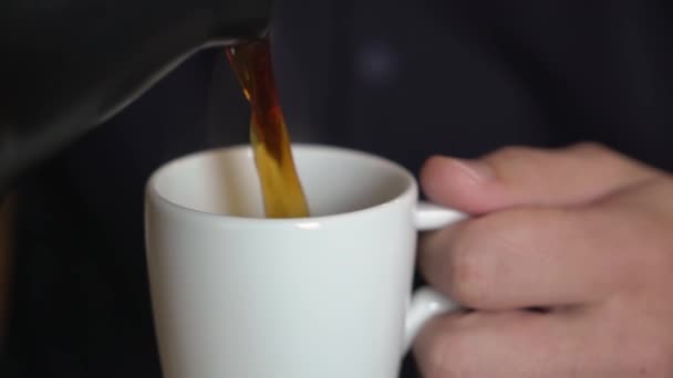 A man pours coffee from a coffee pot or coffee maker into a white cup. - Video, Çekim