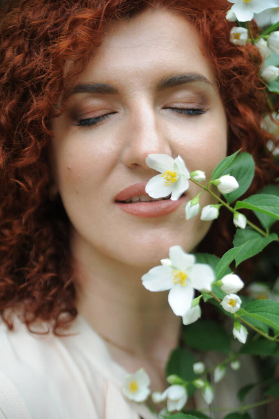 Young beautiful red-haired woman in blossoming flowers garden.  - Photo, Image