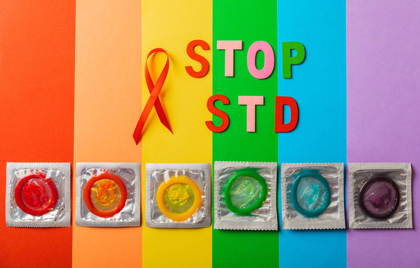 Színes blokkok a "STOP STD" kifejezéssel, piros szalaggal, lapos réteggel.AIDS világnap. Szuper biztonságos eper óvszer, kellemes illattal, sárga háttérrel. A fogamzásgátlók természetes - Fotó, kép