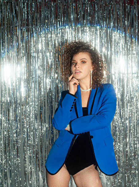 Beautiful curly haired woman in blue jacket posing on sparkling background - 写真・画像