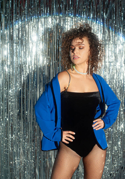 Beautiful curly haired woman in blue jacket posing on sparkling background - Photo, Image
