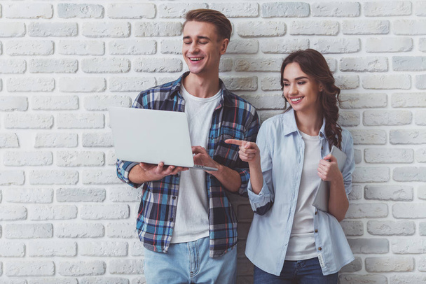 junges schönes Paar hält einen Laptop und ein Tablet auf einem Backsteinhintergrund hoch - Foto, Bild