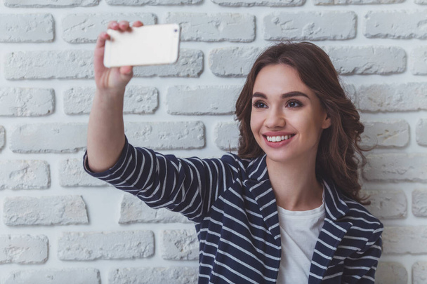 Hermosa mujer joven haciendo autorretrato en un teléfono inteligente sobre un fondo de pared de ladrillo
 - Foto, imagen