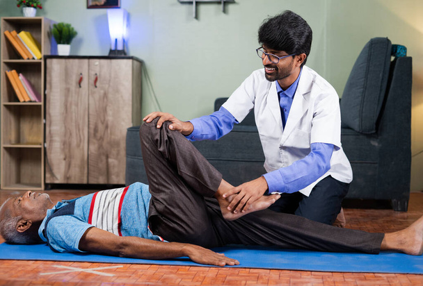 Lääkäri käyttää vanha mies venyttää jalat kotona käsite eläkeläisten kotiin terveystarkastus, polvinivelkipu hoito ja lääketieteellinen hoito tai hoito - Valokuva, kuva