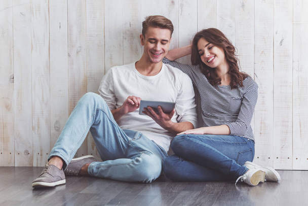 Happy young couple smiling, using tablet, sitting on wooden floor at home - Foto, Imagem