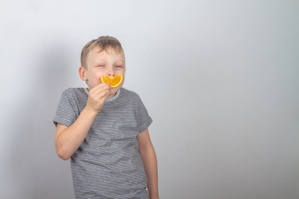 Cheerful caucasian boy smiles made a smile from a slice of orange on a gray background. - Foto, Bild