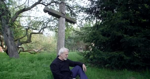 Surullinen vanha harmaa tukkainen mies istuu haudalla iso vanha risti hautausmaalla, surua ja surua läheisten ihmisten menettämisestä, 4k 60p Prores - Materiaali, video