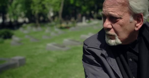 Surullinen vanha harmaa tukkainen mies istuu haudalla hautausmaalla, surua ja surua läheisten ihmisten menettämisestä, 4k 60p Prores - Materiaali, video