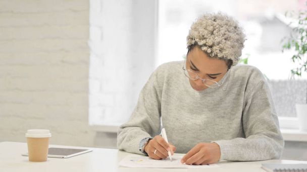 Mujer africana escribiendo en papel en la oficina - Foto, imagen