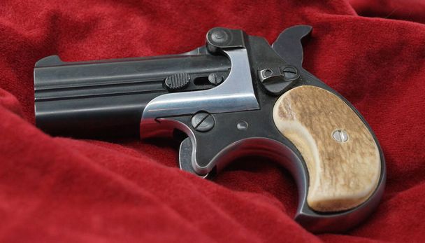 A double barrel derringer style pistol on a red velvet background. This kind of weapon was used by gamblers and women in the past because of its small size. - Valokuva, kuva