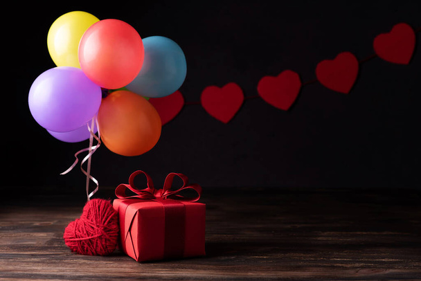 Regalo rojo, corazón, globos de colores sobre fondo de madera oscura, día de San Valentín y tarjeta de felicitación de cumpleaños. - Foto, imagen