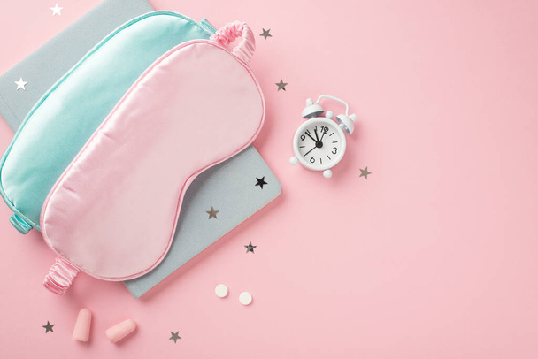 Top view photo of two blue and pink silk sleeping masks small white alarm clock pills earplugs blue reminder and star shaped confetti on isolated pastel pink background with empty space - Фото, изображение