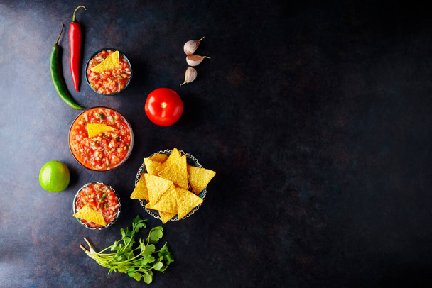 Salsa sauce and nacho chips on a dark background. Mexican salsa sauce and ingredients. Mexican food. Copy space. Top view - Φωτογραφία, εικόνα