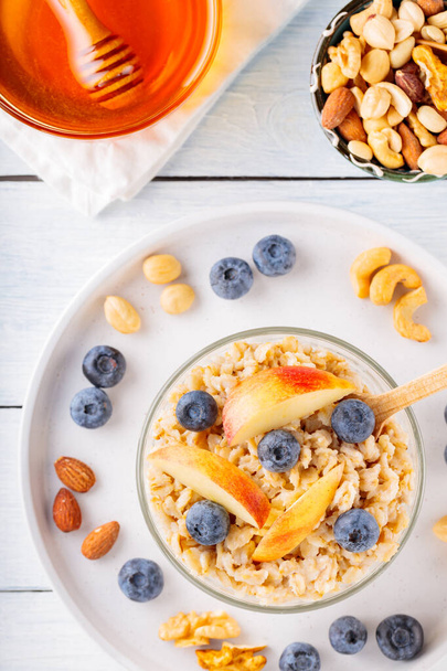 Oatmeal with blueberries and sliced apple in bowl. Oatmeal porridge with berries, nuts and honey on a white boards. Healthy breakfast concept. Top view - Foto, Imagem