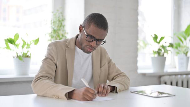 Hombre africano escribiendo en papel en la oficina - Foto, imagen